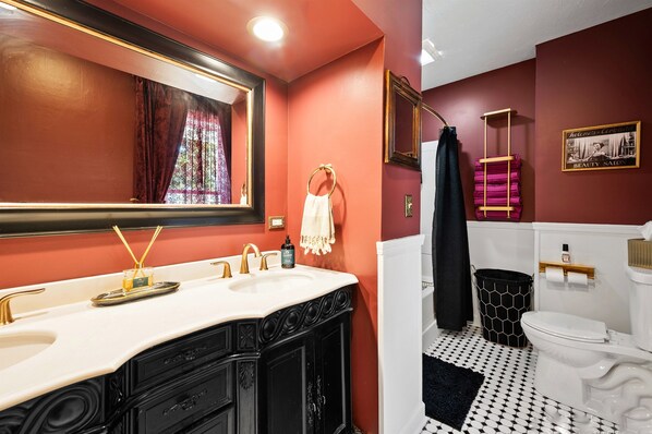 Un baño con pared roja, lavamanos blanco con detalles dorados, piso estampado en blanco y negro, y retrete en blanco y negro.