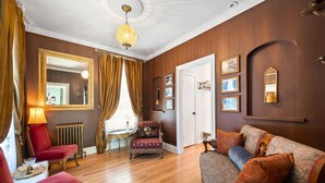 A room with a wooden floor, a red armchair, a patterned sofa, a chandelier, and a large mirror. - Downtown St. Charles: Walk to Bars & Restaurants (St. Charles)