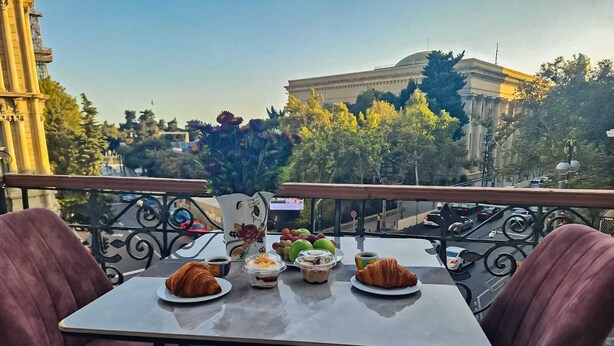 Une table de balcon avec deux chaises, un croissant, une tasse de café et un panier de fruits.