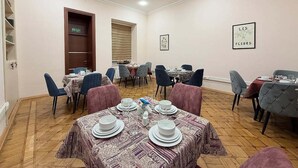 Un espace repas avec plusieurs tables dressées pour les repas, des chaises et une œuvre d’art encadrée accrochée au mur.