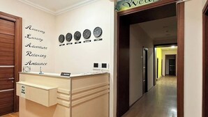 Un comptoir d’accueil surmonté d’une enseigne où est écrit « Bienvenue ». Il y a des horloges au mur et une autre enseigne avec des mots tels que « Incroyable », « Luxe », « Aventure », « Détente » et « Ambiance ».