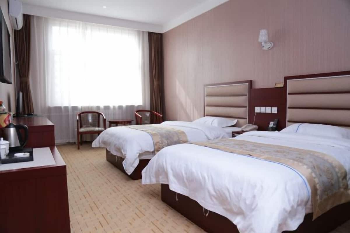 Hotellihuone, jossa on kaksi sänkyä, työpöytä, kahvinkeitin, tuoli ja ikkuna, jossa on verhot.