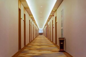 Pasillo de hotel con piso alfombrado, puertas a ambos lados y un accesorio de iluminación en el techo.