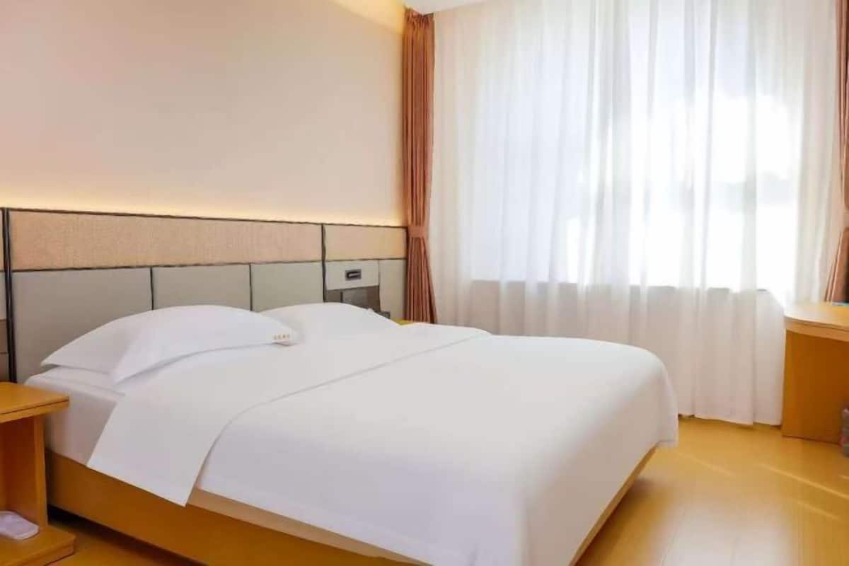 Hotellihuone, jossa on sänky, yöpöytä, lamppu ja ikkuna, jossa on verhot.