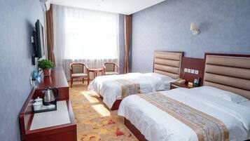 A hotel room with two beds, a desk with a kettle, a chair, and a window with curtains.