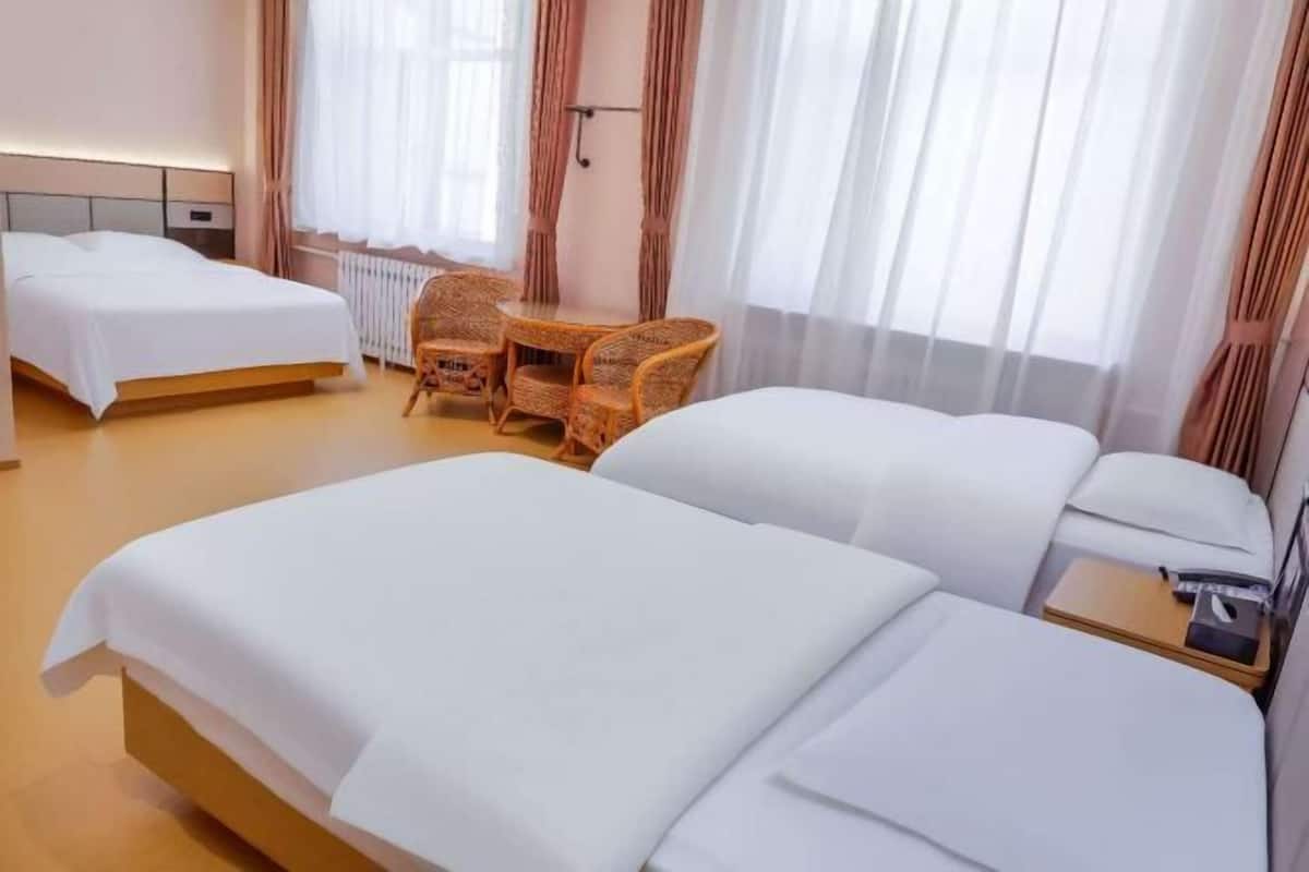 Hotellihuone, jossa on kaksi sänkyä, pieni pöytä tuoleineen, yöpöytä ja patteri.