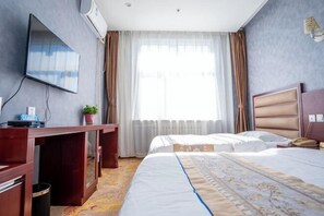 Une chambre d’hôtel équipée d’un bureau, de deux lits, d’une télévision et d’une grande fenêtre avec des rideaux.