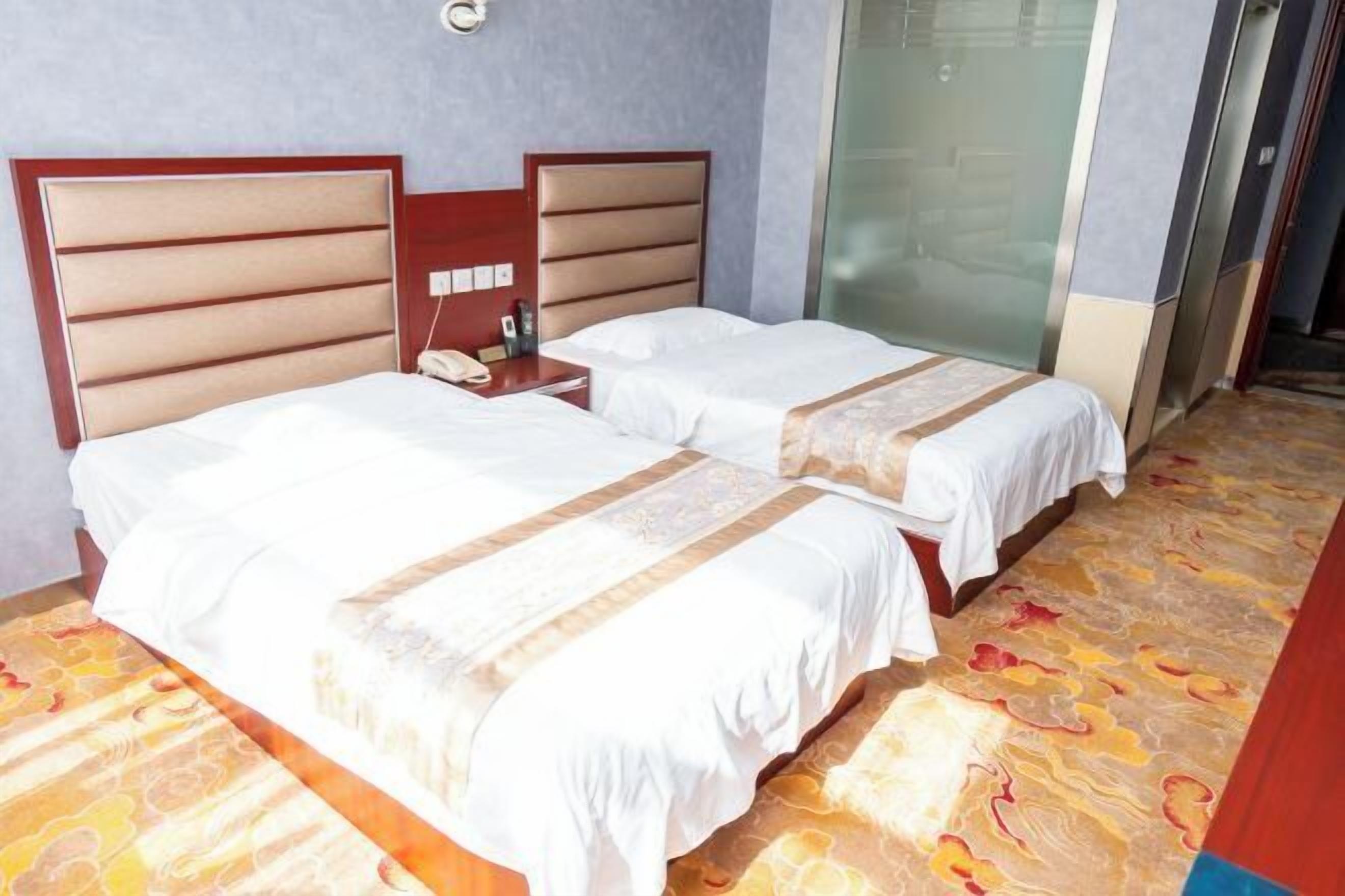 A hotel room with two beds, a bedside table with a phone, and a glass shower enclosure.