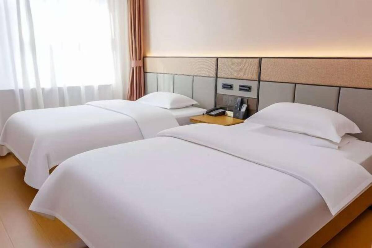 Hotellihuone, jossa on kaksi sänkyä, yöpöytä, puhelin ja lamppu.