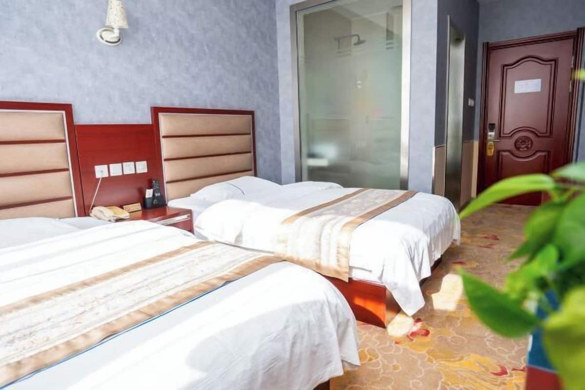 Hotellihuone, jossa on kaksi sänkyä, puinen pääty, yöpöytä lampun kanssa ja liukuovi.