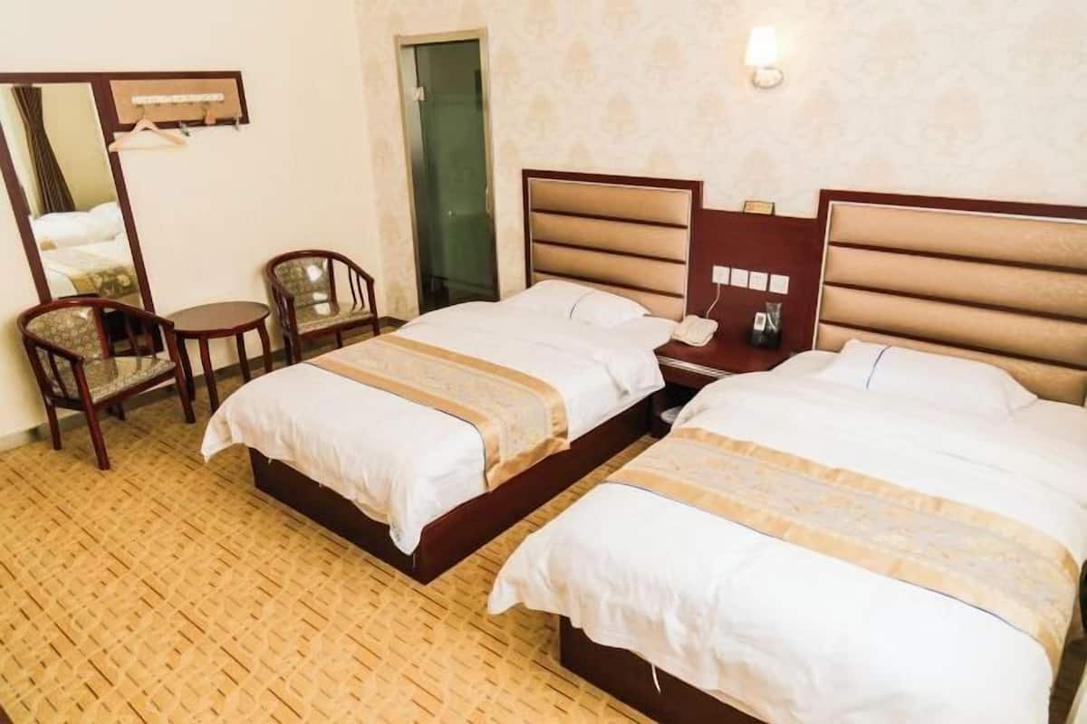 Hotellihuone, jossa on kaksi sänkyä, pieni pöytä, tuoli, peili ja yöpöytä, jossa on lamppu.