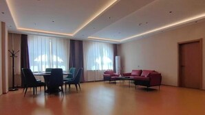 A spacious room with a dining table, chairs, a sofa, and a large window with curtains. - YunLong HOTEL (Ongniud Banner)
