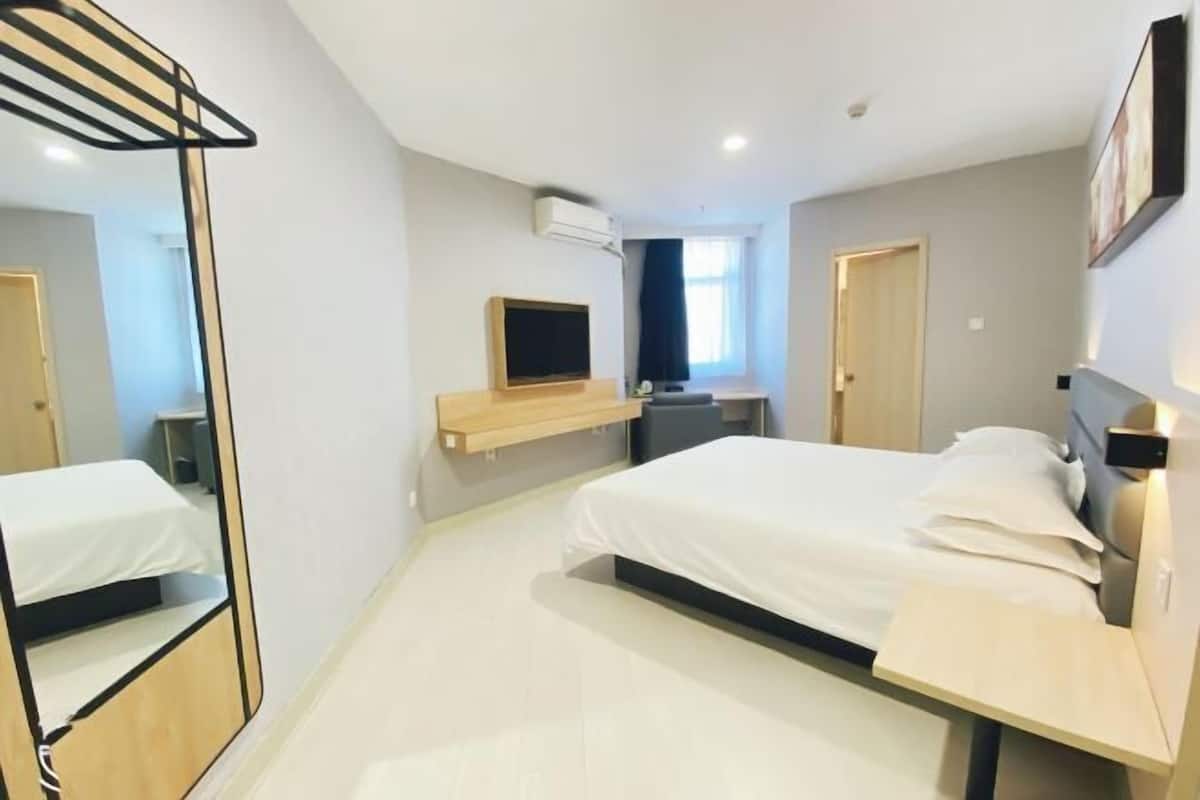 A modern hotel room with a large bed, a TV mounted on the wall, a small desk, and a mirror.