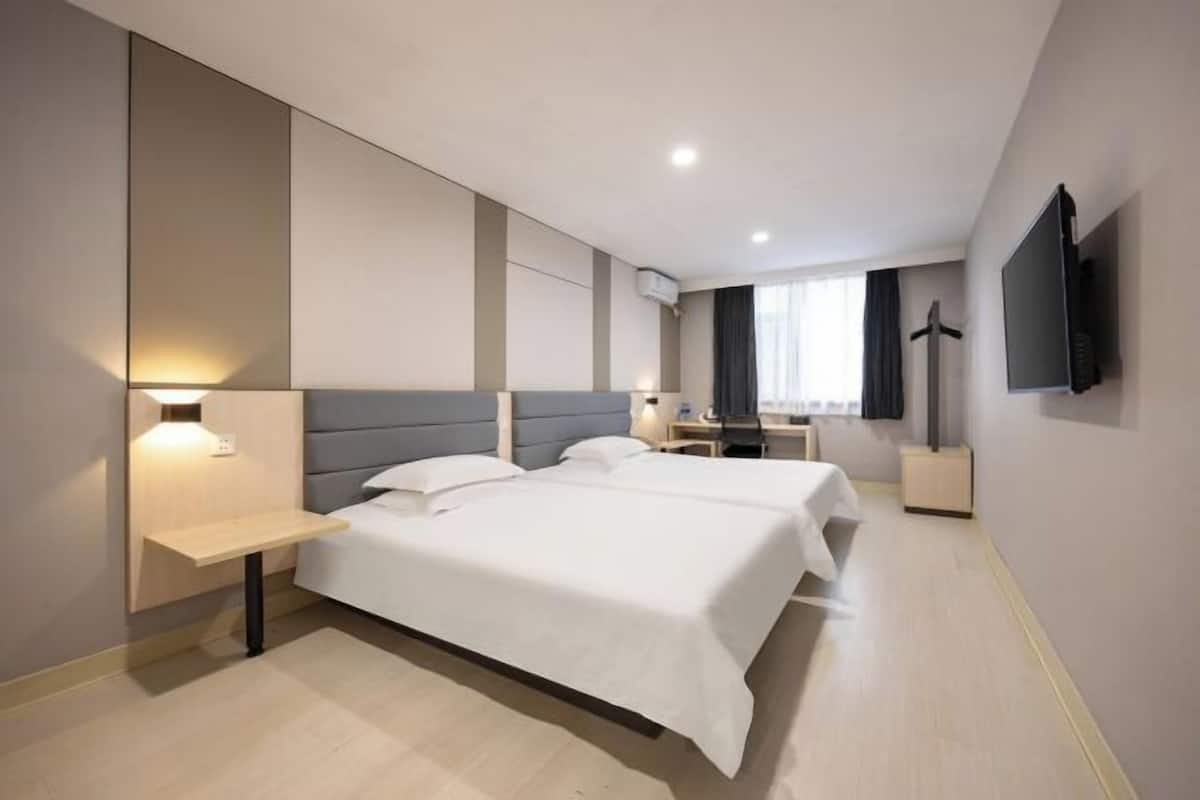A modern hotel room with two beds, a desk, a chair, a flat-screen TV, and a window with curtains.