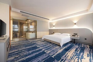 Una habitación de hotel moderna con una cama grande, un televisor de pantalla plana, un box de ducha de vidrio y una alfombra azul estampada.