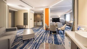 A hotel room with a sofa, a small table, a TV, and a bathroom with a sink and mirror. - Jinzhou Star Hotel (Jinzhou Luoyang Road) (Jinzhou)