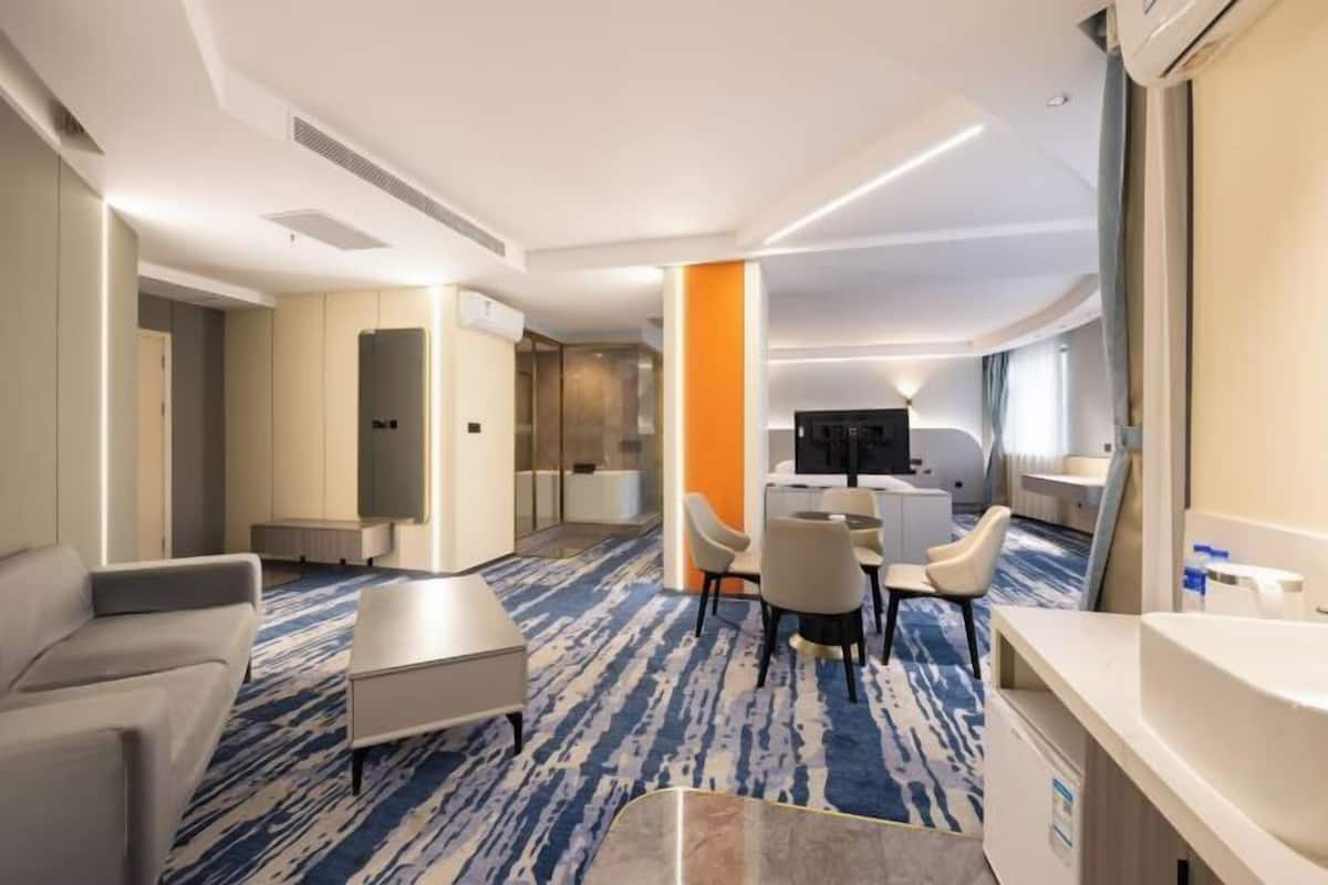 A hotel room with a sofa, a small table, a TV, and a bathroom with a sink and mirror.