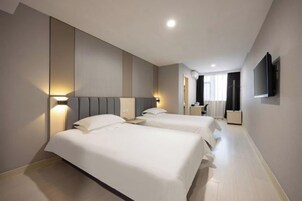 Habitación de hotel con dos camas, una televisión montada en la pared y una mesita de noche con lámpara.