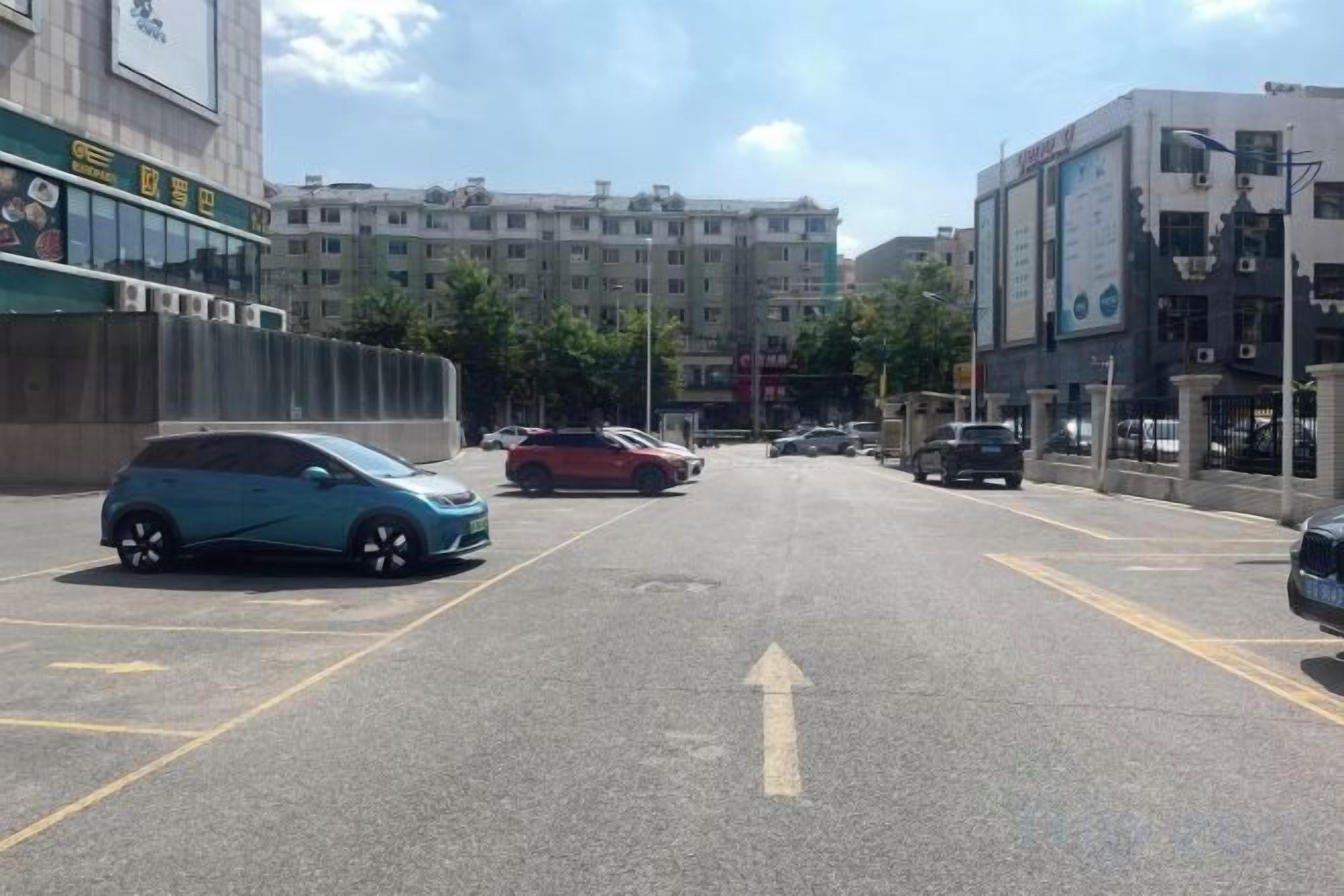 A street with parked cars and buildings in the background.