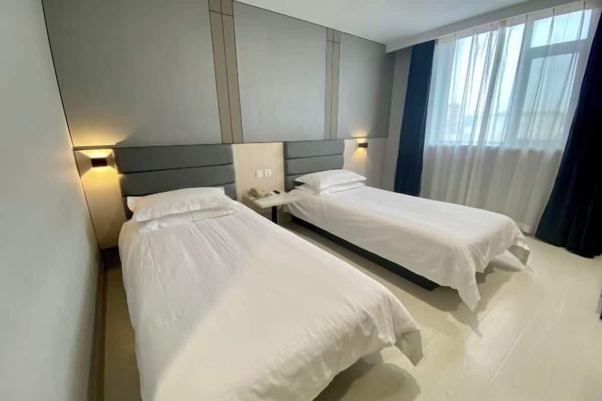 A hotel room with two single beds, a modern headboard, and a large window with curtains.
