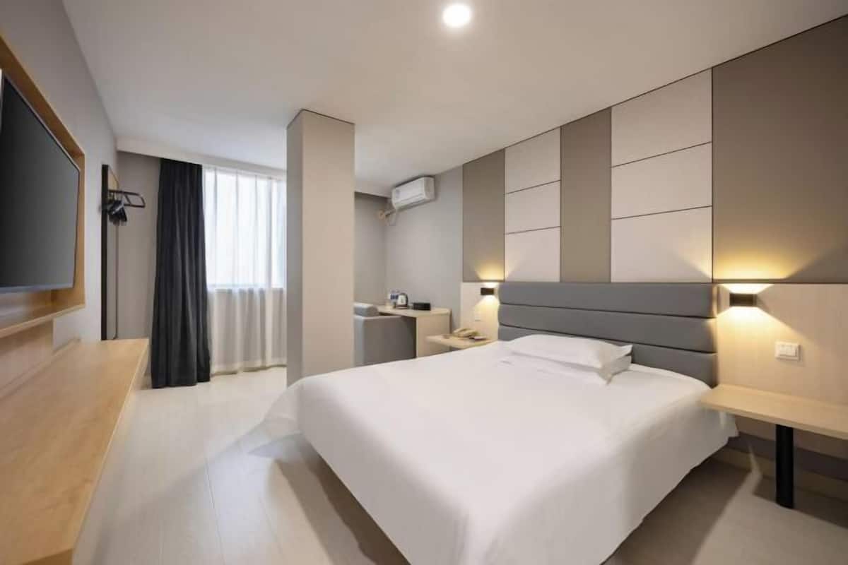 A modern hotel room with a large bed, bedside tables, a flat-screen TV, a desk, and a window with curtains.