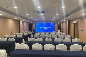 Une salle de conférence avec des rangées de tables et de chaises, un pupitre et un écran de présentation.