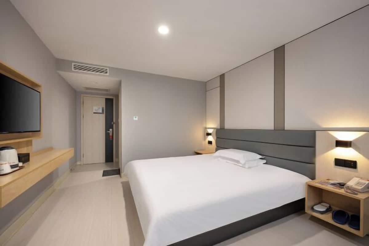 A modern hotel room with a large bed, bedside tables, a flat-screen TV, and a built-in heater.