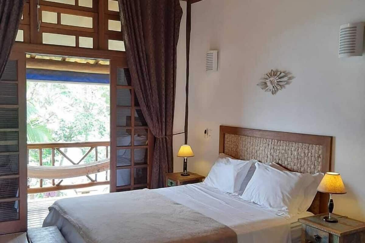 Una cama con cabecera de madera, dos lámparas de noche y un banco al pie de la cama.