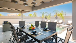 An outdoor dining area with a pool, dining chairs, and a table set for two. - Hollywood 3 Bedroom Villa with private pool (Ampelokipoi)