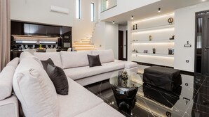 A modern living room with a sofa, a coffee table, and a staircase leading to an upper level. - Hollywood 3 Bedroom Villa with private pool (Ampelokipoi)
