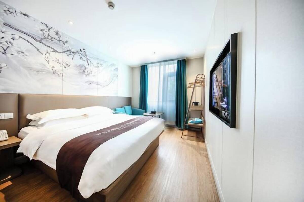 A modern hotel room with a large bed, a desk, a chair, a TV, and a painting on the wall.