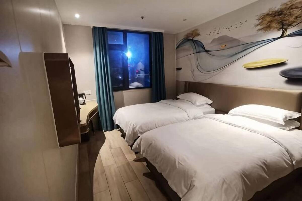 A hotel room with a bed, a desk, a window with curtains, and a wall decoration.