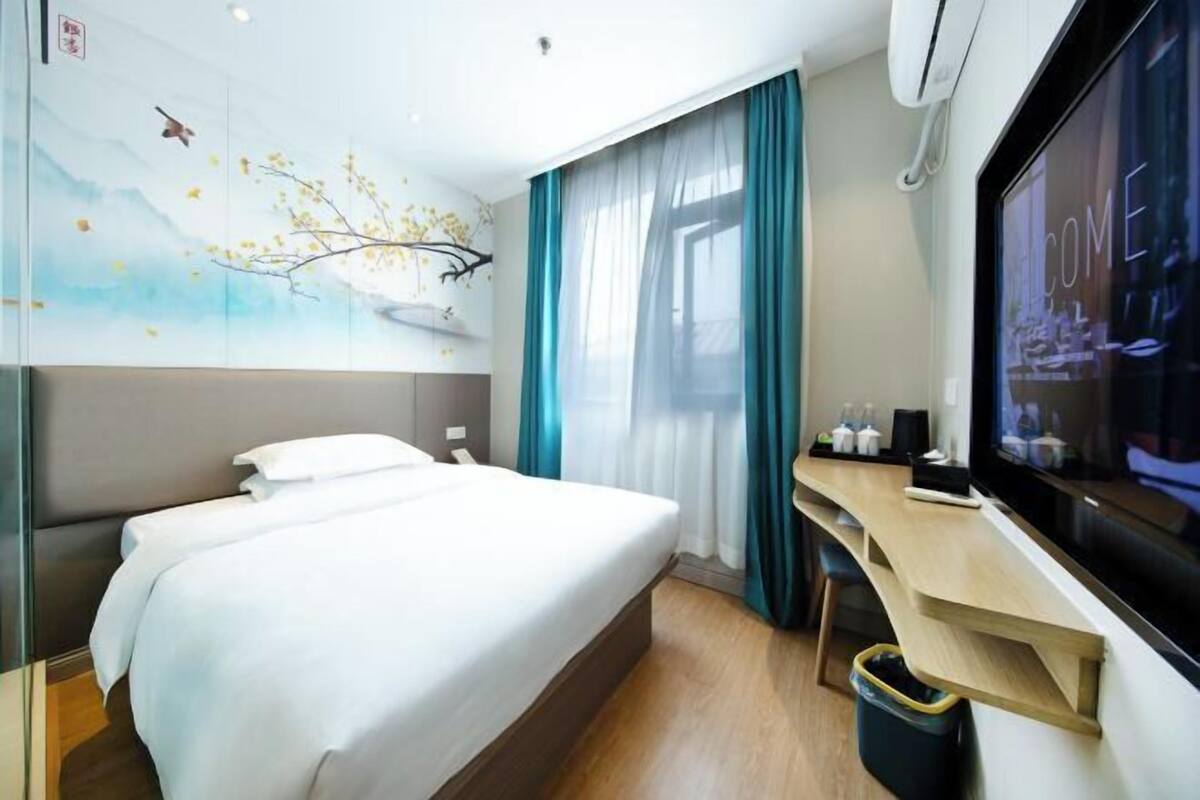 A hotel room with a bed, a desk, a TV, and a wall mural.