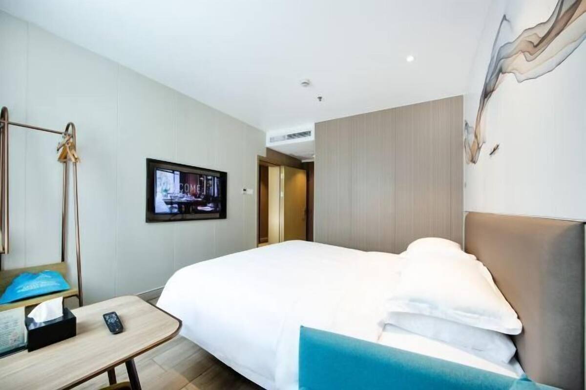 A hotel room with a bed, a television, a desk with a phone, and a wall-mounted artwork.