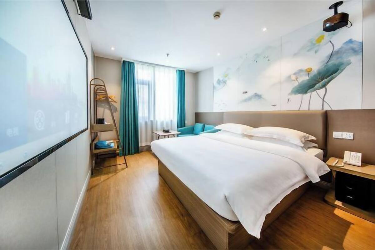 A modern hotel room with a large bed, a desk, a chair, and a painting on the wall.