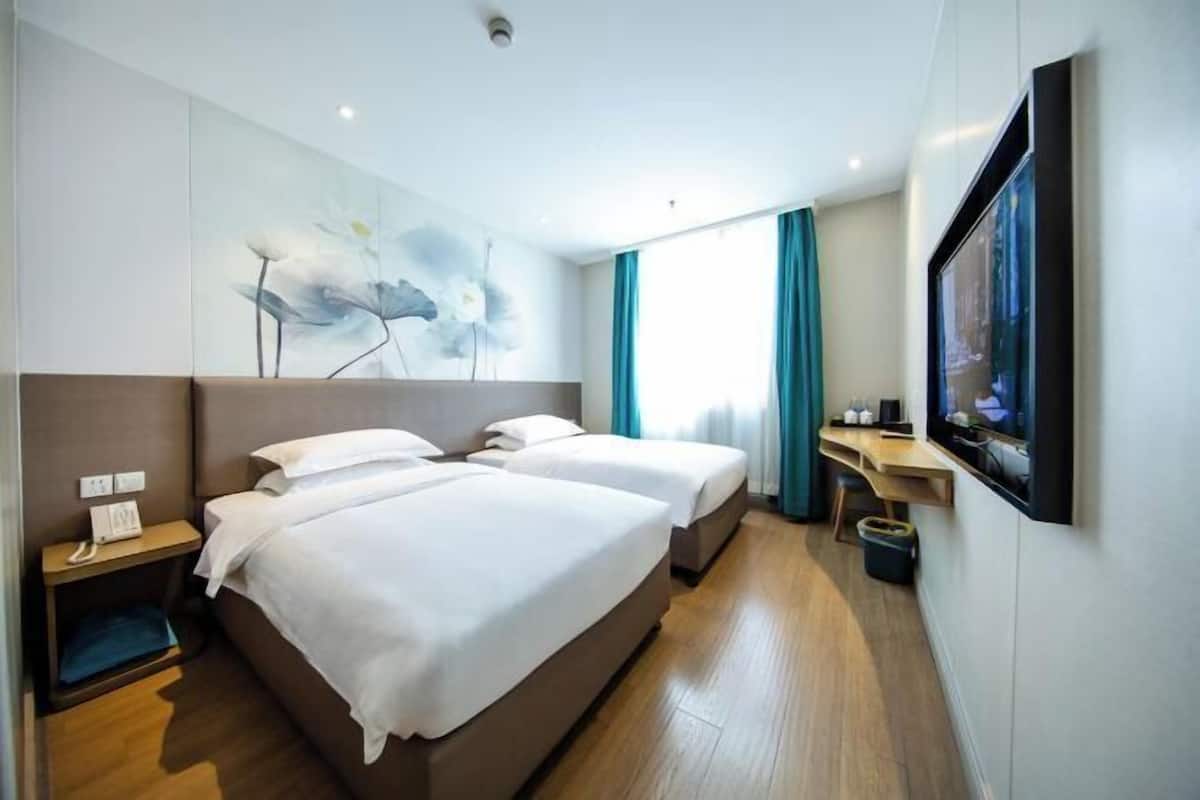 A hotel room with two beds, a desk, a TV, and a painting on the wall.
