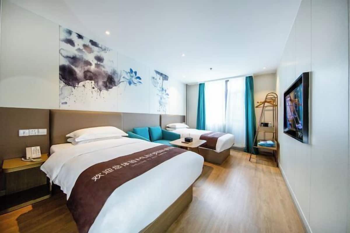 A modern hotel room with a large bed, a sofa, a desk, and a painting on the wall.