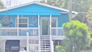 A blue house with a balcony, a mural of sea creatures, and a white fence.