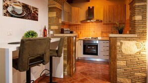 A kitchen with a stone archway, wooden cabinets, a stove, and a dining area with a chair and table. - MATEO Studio with Terrace (Rovinjsko Selo)