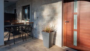 A stone wall exterior, a wooden door with glass panels, a dining table with chairs, and a potted plant. - MATEO Studio with Terrace (Rovinjsko Selo)