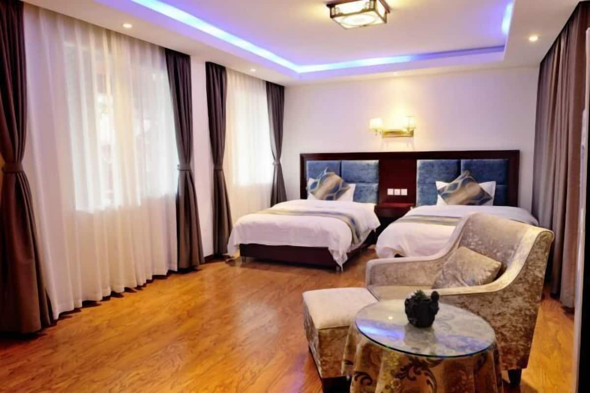 Habitación de hotel con dos camas, un sofá, una mesita y una lámpara en el techo.