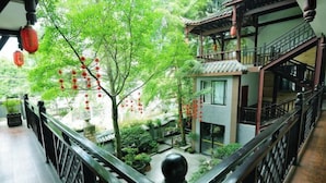 Un bâtiment traditionnel à plusieurs étages, doté d’un balcon, d’un petit jardin et de lanternes rouges.