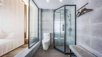 A modern bathroom with a glass shower enclosure, a toilet, and a bench.