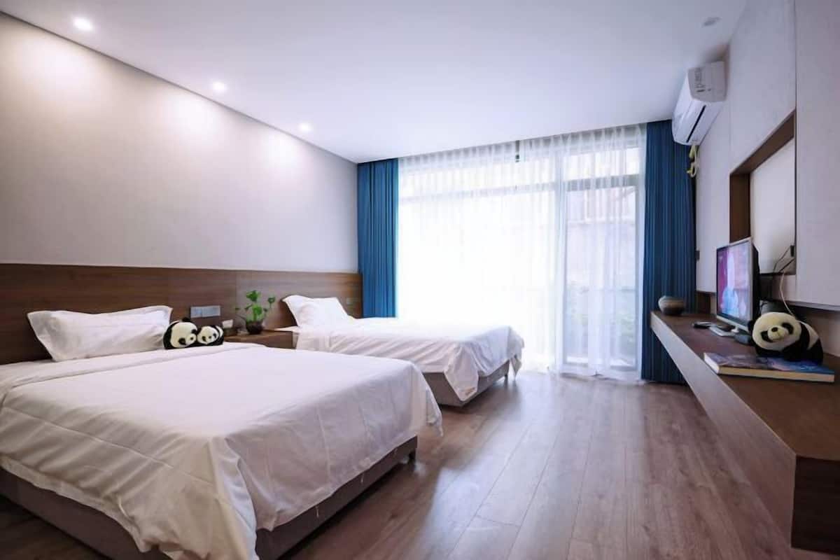 Una habitación de hotel con dos camas, un escritorio con computadora y una ventana con cortinas.