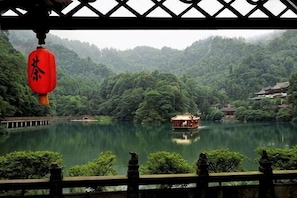 A serene lake with a traditional boat, surrounded by lush greenery and a wooden bridge.