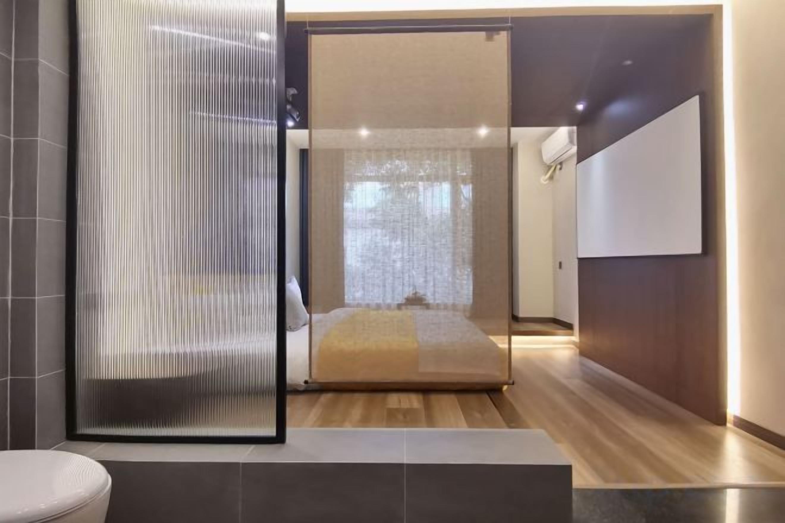 A modern bedroom with a large bed, a glass partition, and a view of a cityscape.