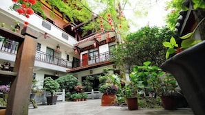 Une cour avec des plantes en pot, un balcon en bois et la façade d’un immeuble.