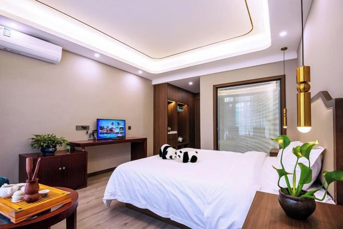A modern hotel room with a bed, a desk, a television, and a window with blinds.