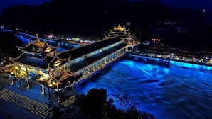 Il s’agit d’un bâtiment traditionnel chinois, caractérisé par une structure longue et étroite et des toits richement décorés, situé au bord d’une rivière.