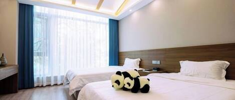 A hotel room with two beds, a wooden headboard, a bedside table, and a large window with curtains.